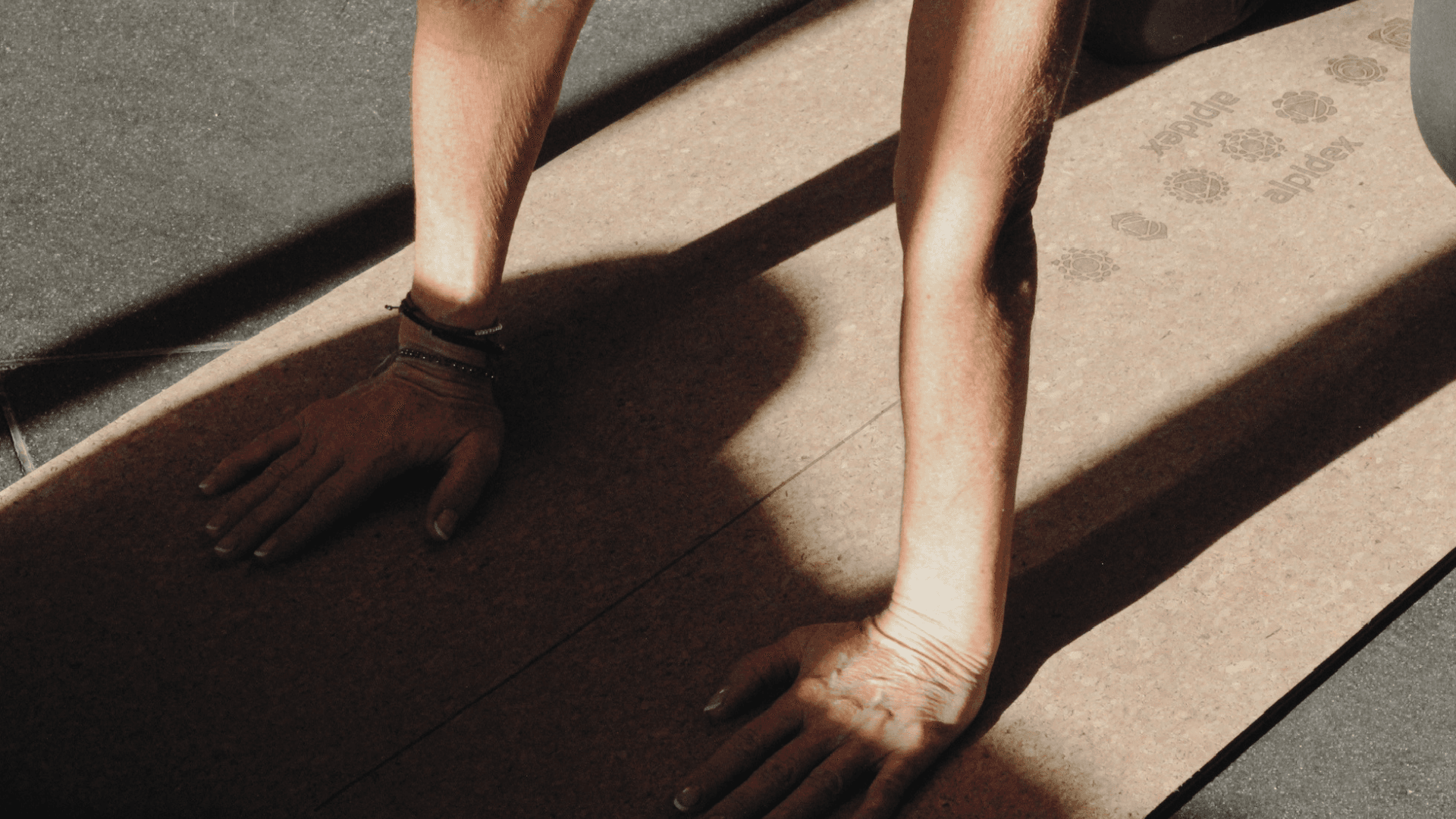A woman´s hands in table top practicing yoga on a sundappled cork yoga mat