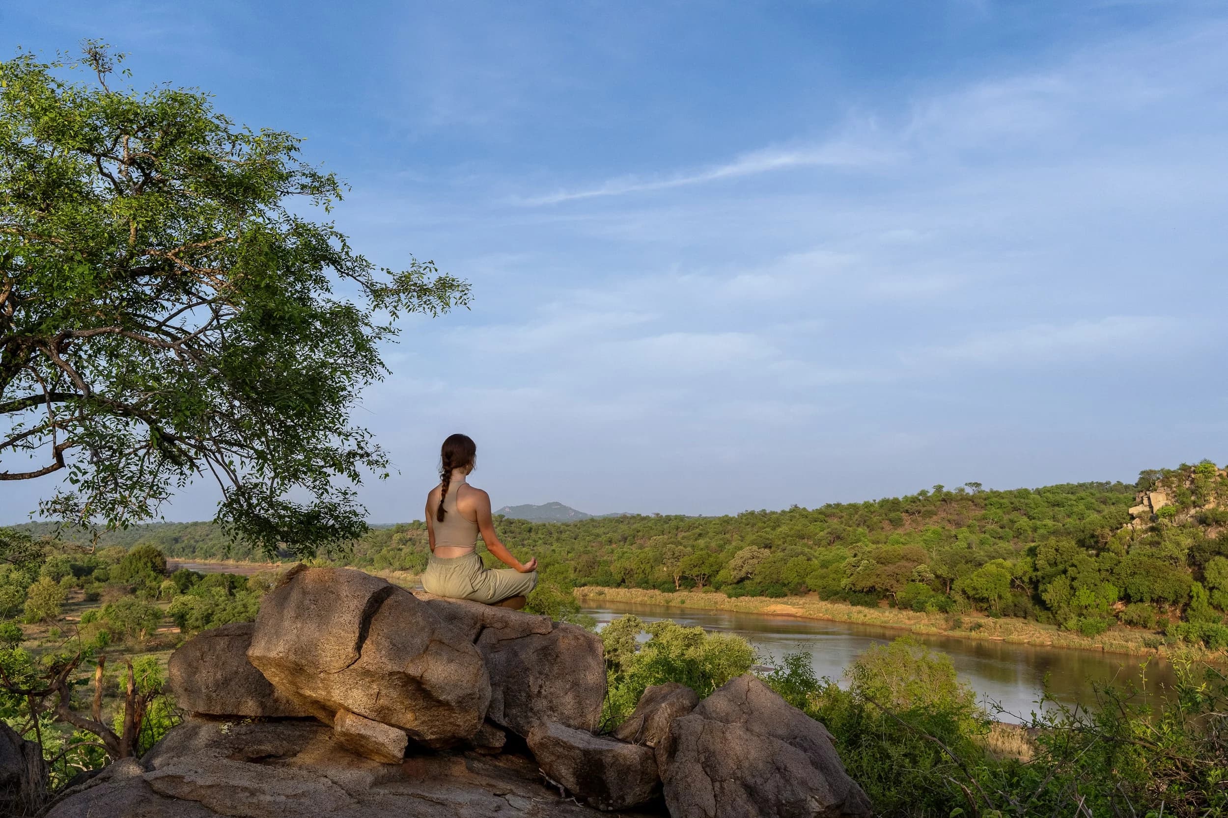 A guest meditating on the rocks above the Sashwa river under a bright blue sky
